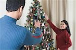 Man taking a picture of his wife decorating Christmas tree