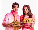 Paar feiern Holi mit Platten von Süßspeisen
