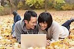 Couple utilisant un ordinateur portable et se trouvant dans les feuilles d'automne