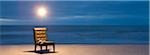 Light bulb illuminated over chair with open book on beach at night