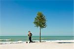 Garçon debout avec une pelle à côté des arbres plantés sur la plage