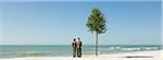 Children standing with shovels beside tree planted on beach