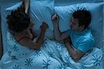 Couple lying together in bed, woman watching man sleeping