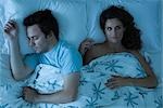 Couple lying together in bed, woman awake looking away contemplatively
