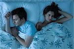 Couple lying together in bed, woman restlessly awake looking away