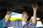 Mechanic working on underside of car elevated on hydraulic lift