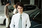 Car salesman in car dealership showroom, potential buyers in background