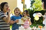 Boy opening gift and smiling with pleasure at birthday party