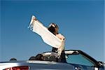 Woman standing up in convertible with arms outstretched