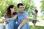 Couple relaxing together outdoors, woman looking over shoulder at son playing in background