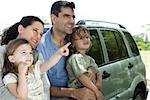 Family leaning against car, all looking as daughter points at something in distance