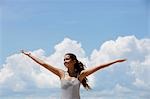 young woman lifting up her arms with blue sky and clouds background