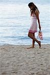 Junge Frau zu Fuß am Strand mit rosa Blumen