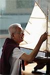 mature man working on model sail boat and smiling
