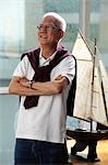 mature man folding his arms and smiling in front of model sail boat