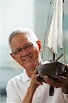 head shot of mature man holding model sail boat and smiling