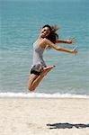 glückliche junge Frau springt in die Luft am Strand