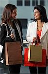 deux femmes tenant des sacs à provisions et en regardant l'autre souriant.