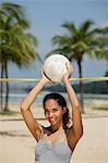 Junge Frau hält Volleyball und lächelnd am Strand