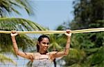 Junge Frau hält Volleyballnetz am Strand