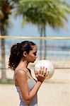Profil anzeigen: junge Frau hält Volleyball am Strand