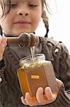 Girl taking organic honey out of jar with honey dipper
