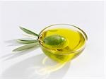 A green olive in a small glass dish of olive oil