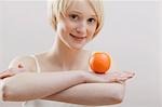 Young woman balancing an orange on folded arms