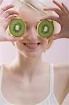 Young woman with two kiwi fruit halves in front of her face