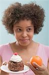 Jeune femme indécise entre le gâteau et orange