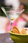 Martini with green olive, crackers, woman in background