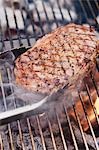 Beef steak on smoking barbecue with barbecue tongs