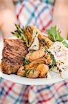 Woman holding plate of grilled steak and accompaniments