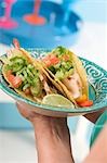 Woman holding plate of two chicken tacos