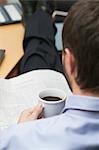 Businessman drinking coffee while reading newspaper in office