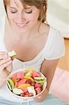 Woman eating wedge of apple from fruit salad