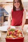 Young woman holding roasted root vegetables in roasting dish