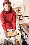 Young woman taking freshly baked apple tart out of oven