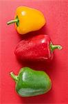 Different coloured peppers with drops of water on red background