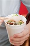 Woman holding paper cup of Asian noodle soup