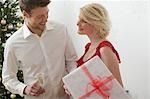 Woman holding large Christmas parcel, man holding glass of wine