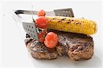 Grilled T-bone steak, corn on the cob, tomatoes, grill tongs