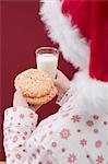 Woman in Father Christmas hat holding cookies & glass of milk