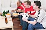 Three football fans with nibbles and beer watching TV