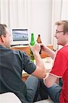 Two football fans clinking bottles of beer while watching TV