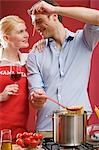 Couple cooking spaghetti & tomatoes, woman holding glass of wine