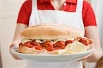 Woman holding giant sandwich filled with meatballs & tomato sauce