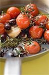 Fried cherry tomatoes with garlic and olives in frying pan