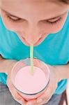 Young woman drinking strawberry milk through straw (close-up)