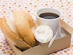 Sesam-Bagel mit Creme fraiche im Karton, Tasse Kaffee